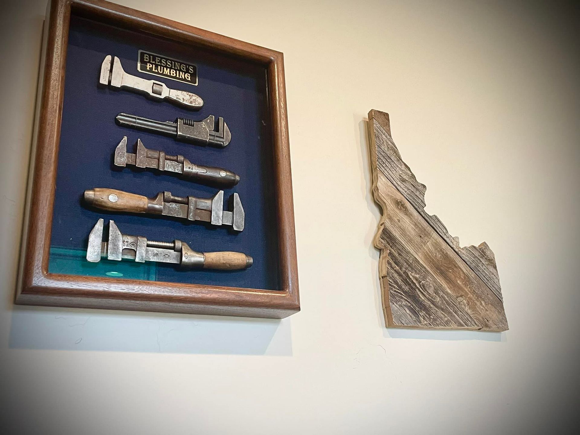 Shadowbox with antique wrenches and wooden Idaho-shaped artwork on a light beige wall.