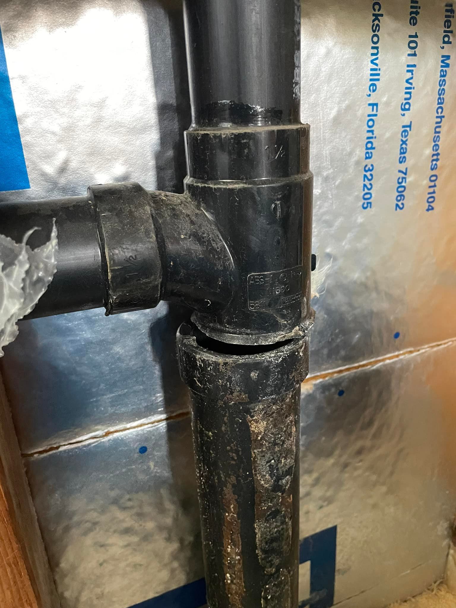Black PVC drain pipes joined with a tee fitting; one pipe appears damaged and cut.