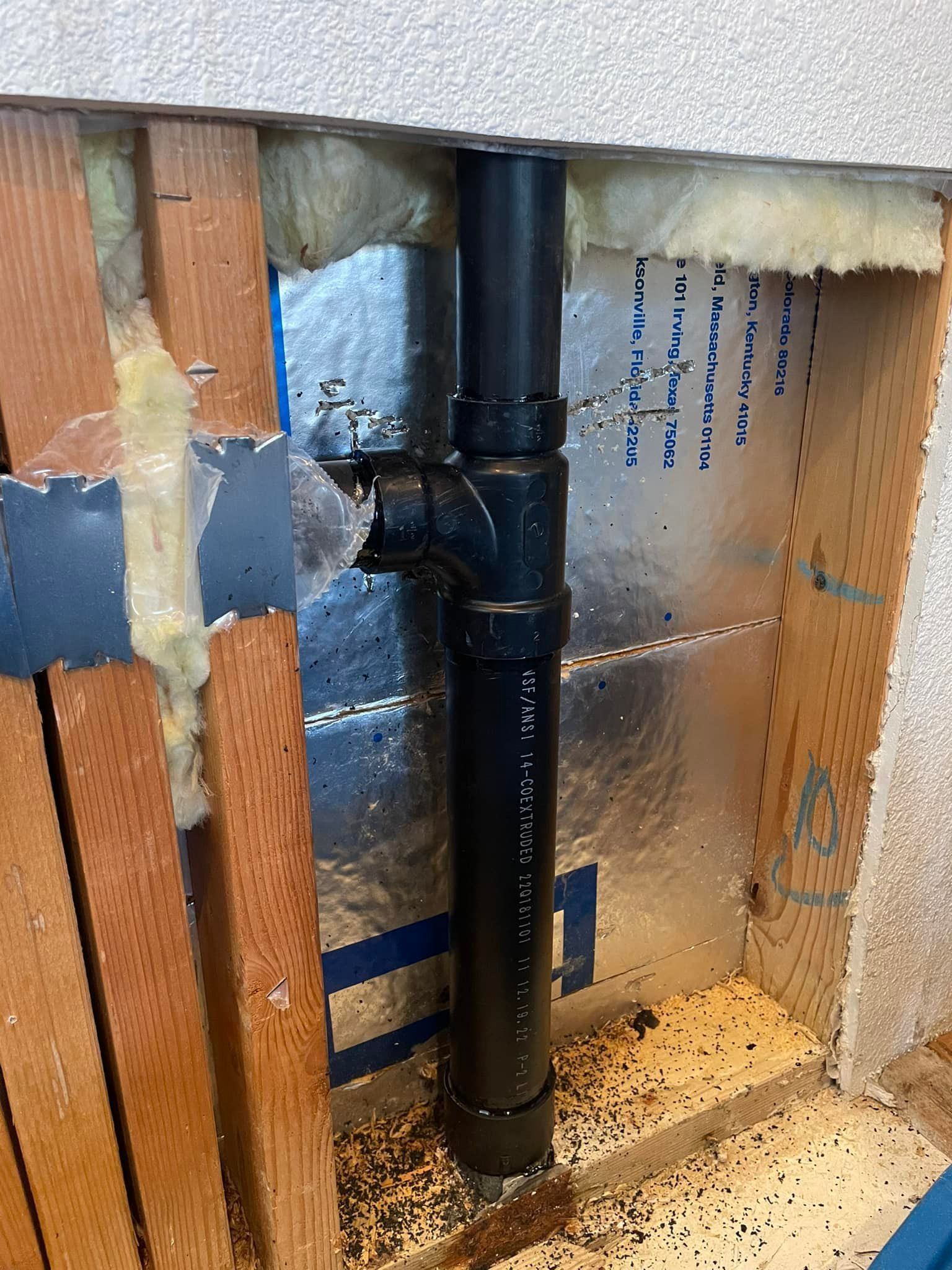 Black plumbing pipes installed in a wall cavity, with insulation and wood framing visible.