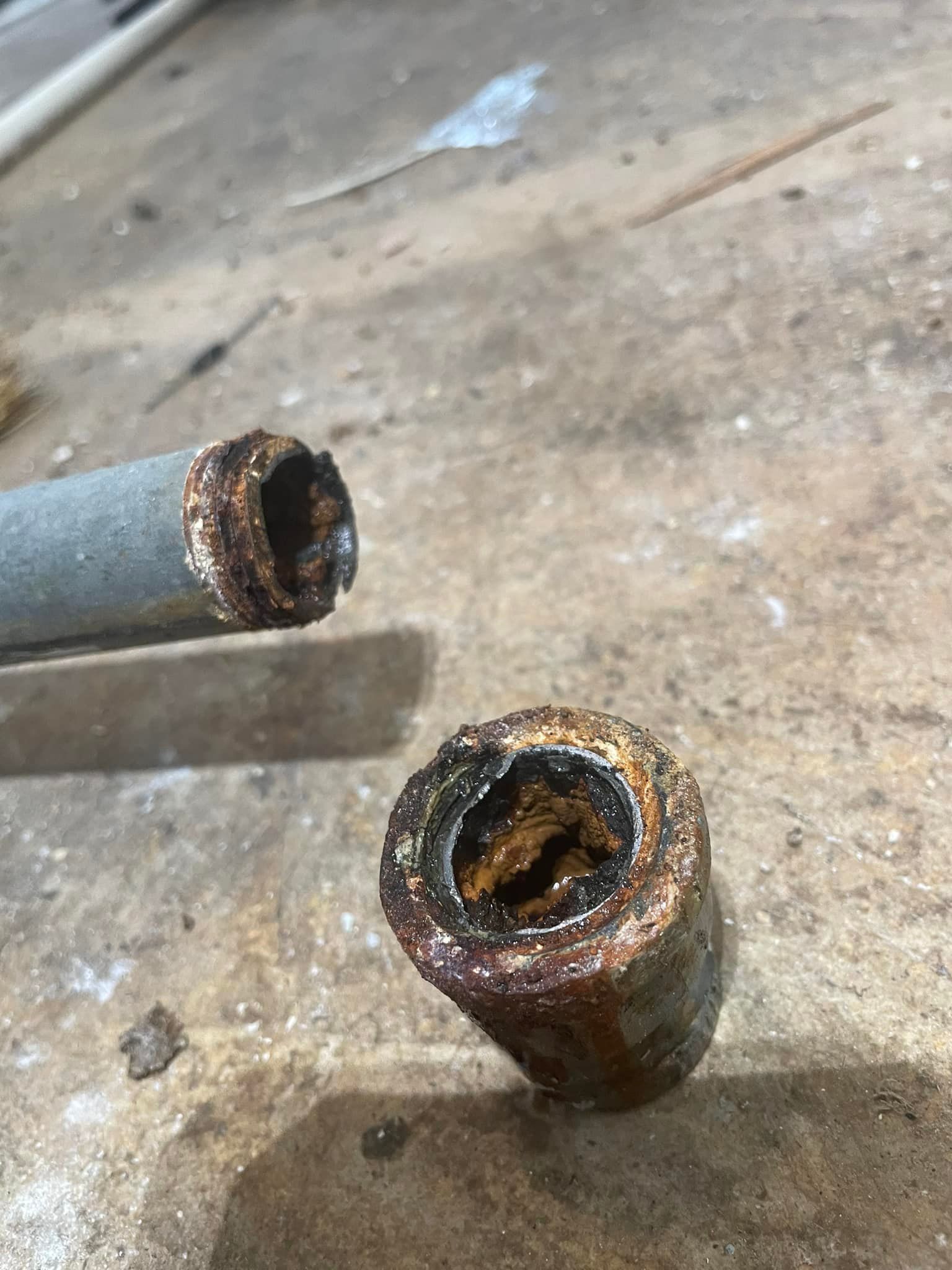 Two corroded pipes cut open, revealing rust and mineral buildup inside.