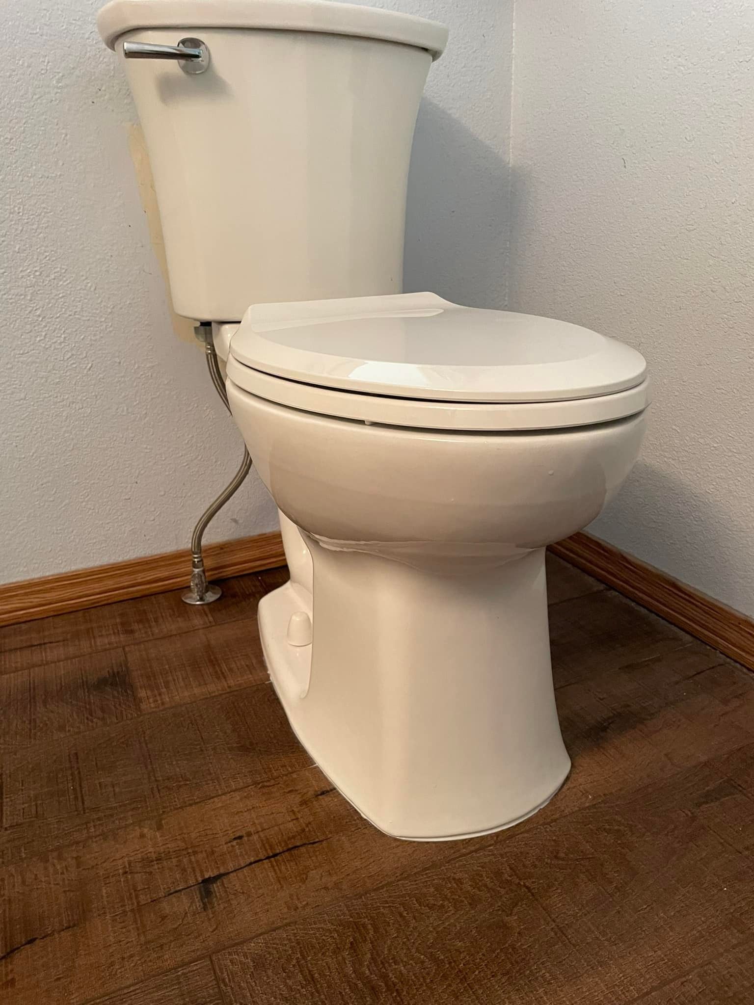 Beige toilet in a bathroom with dark wood-look flooring and light patterned walls.