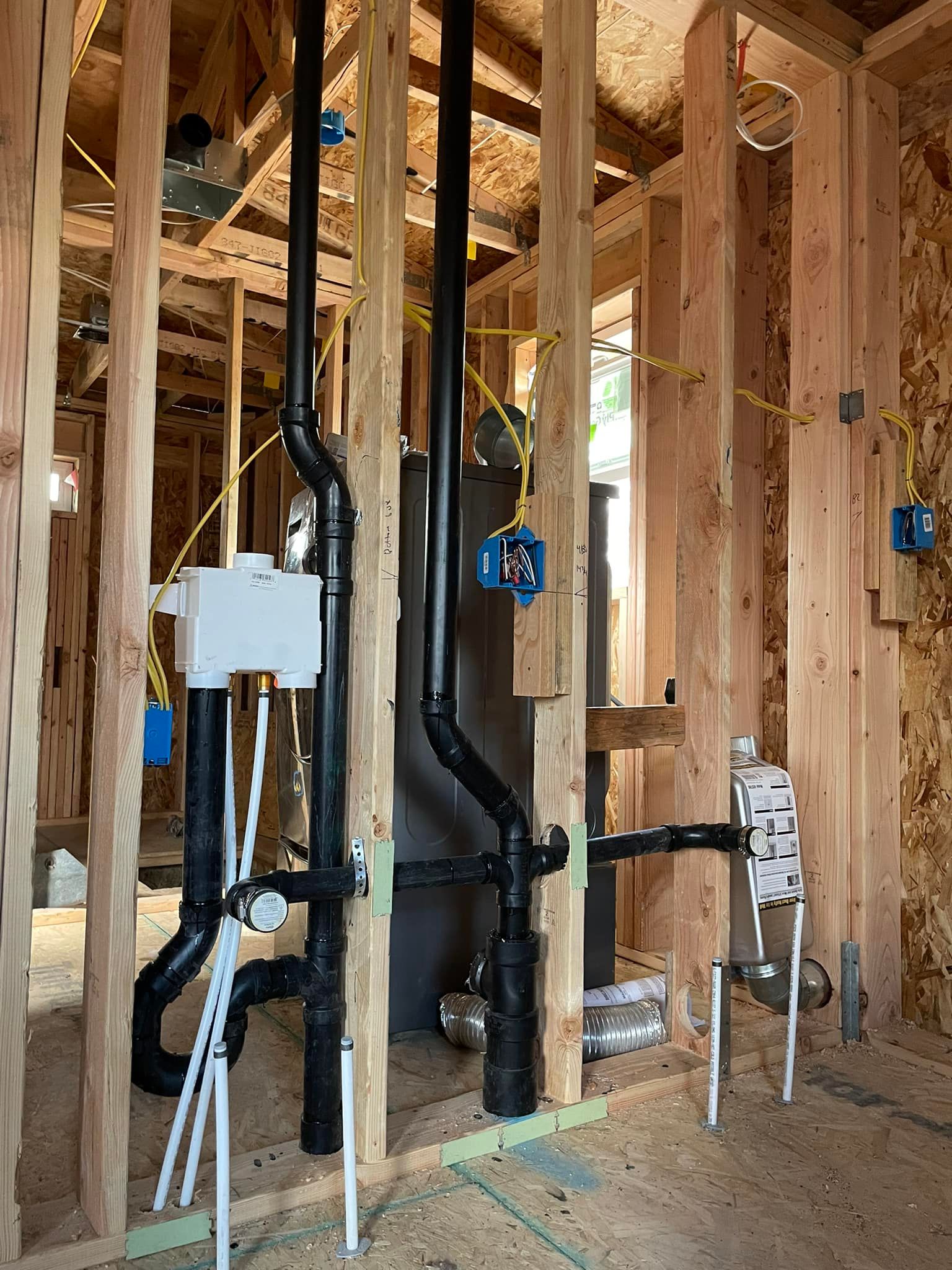 Framing of plumbing and electrical work inside a house under construction; black pipes, blue electrical boxes, and yellow wires.