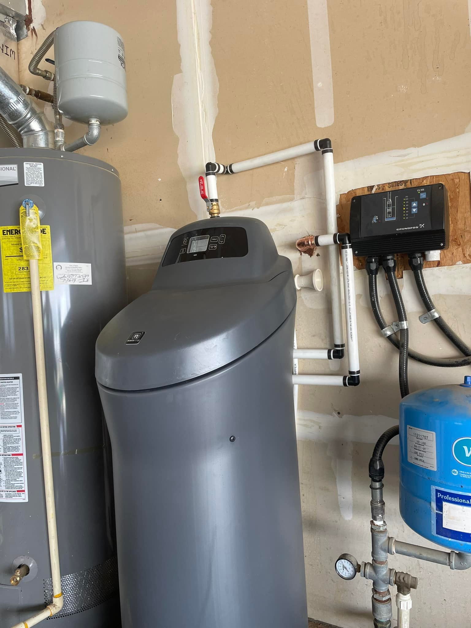 A water softener system and water heater are installed on a wall in a garage.