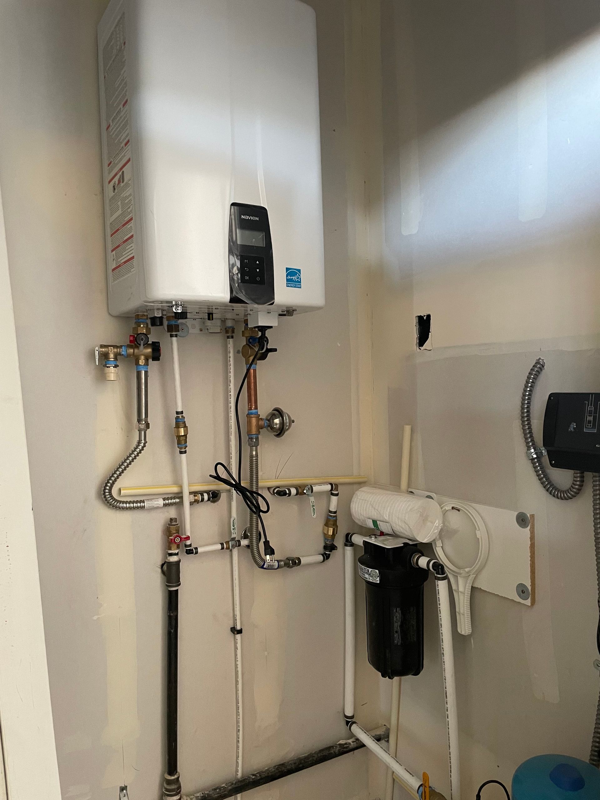 White tankless water heater with pipes and filter installed on a wall.