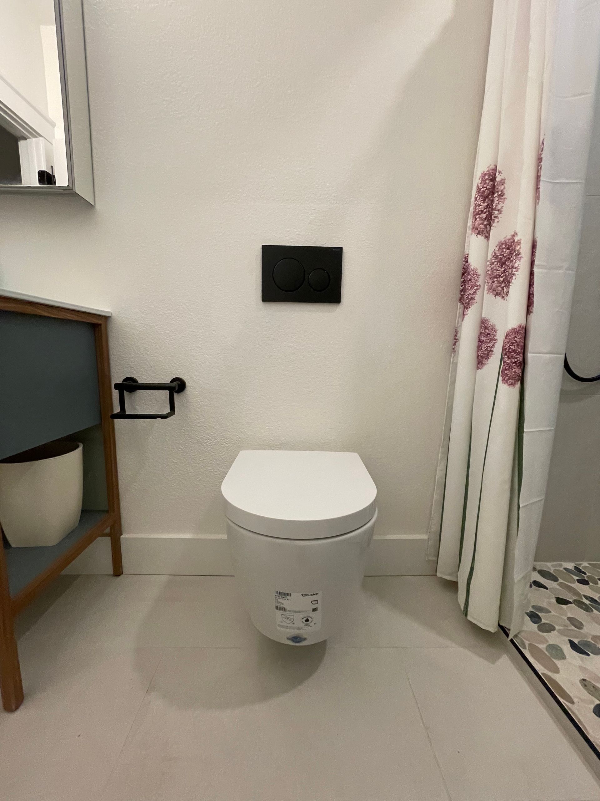 Bathroom with a white toilet, black flush button, and patterned shower curtain.