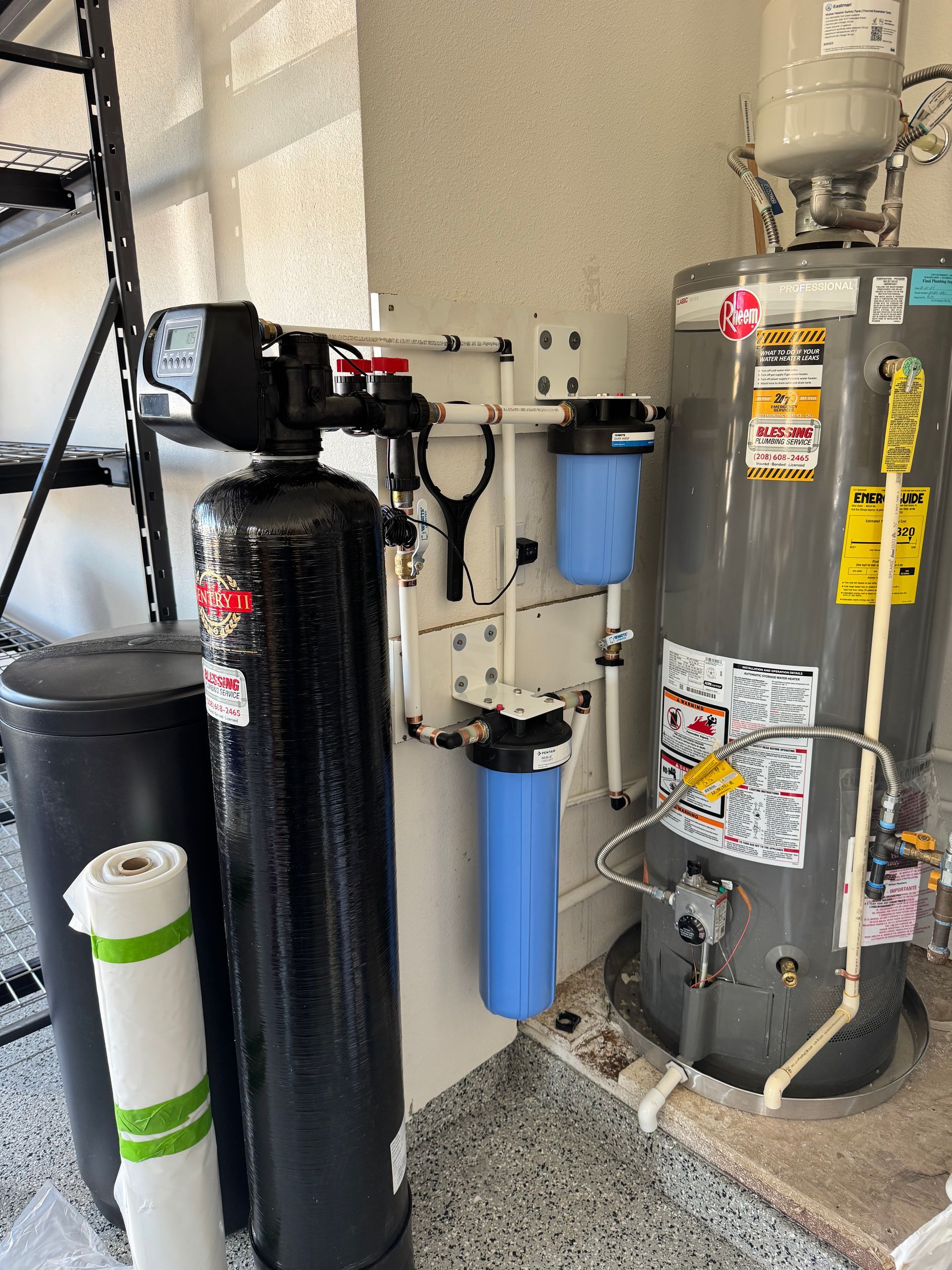 Water filtration system and water heater in a garage, with blue and black tanks and white pipes.