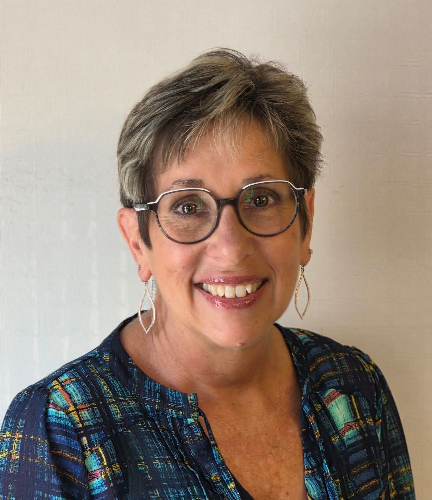 A woman wearing glasses and earrings is smiling for the camera.