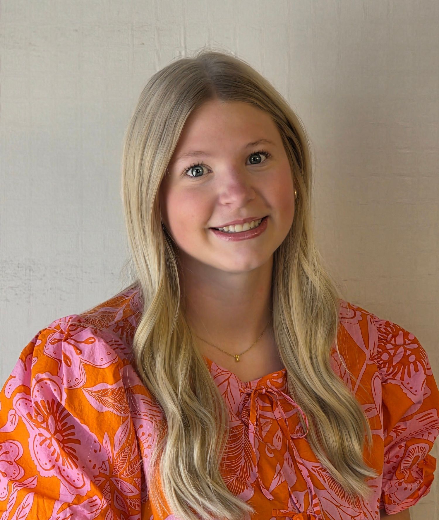 A young woman wearing a pink and orange shirt is smiling for the camera.