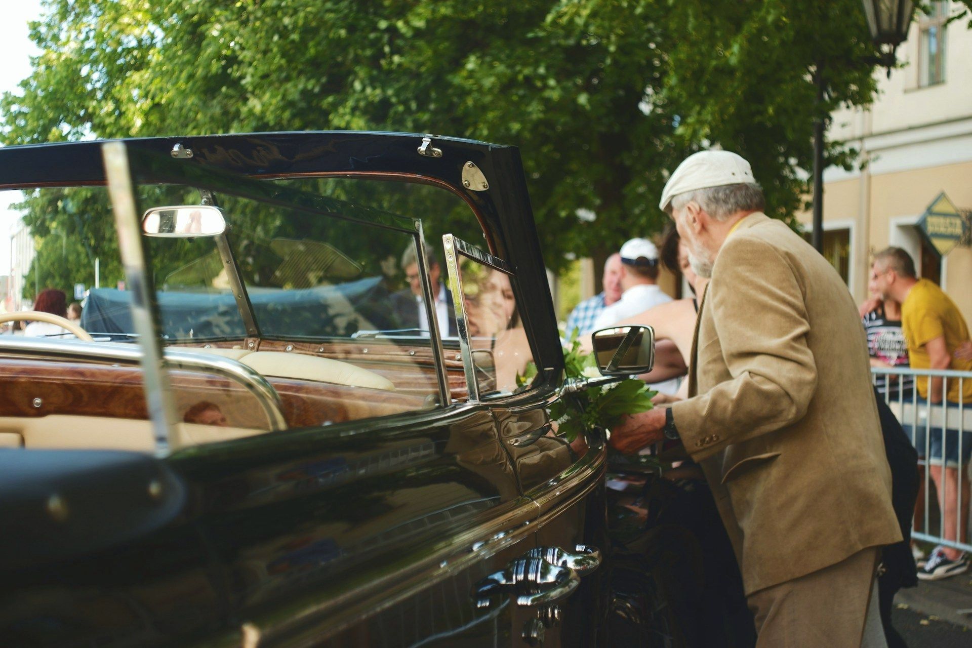 An elderly man is standing next to an old car. 