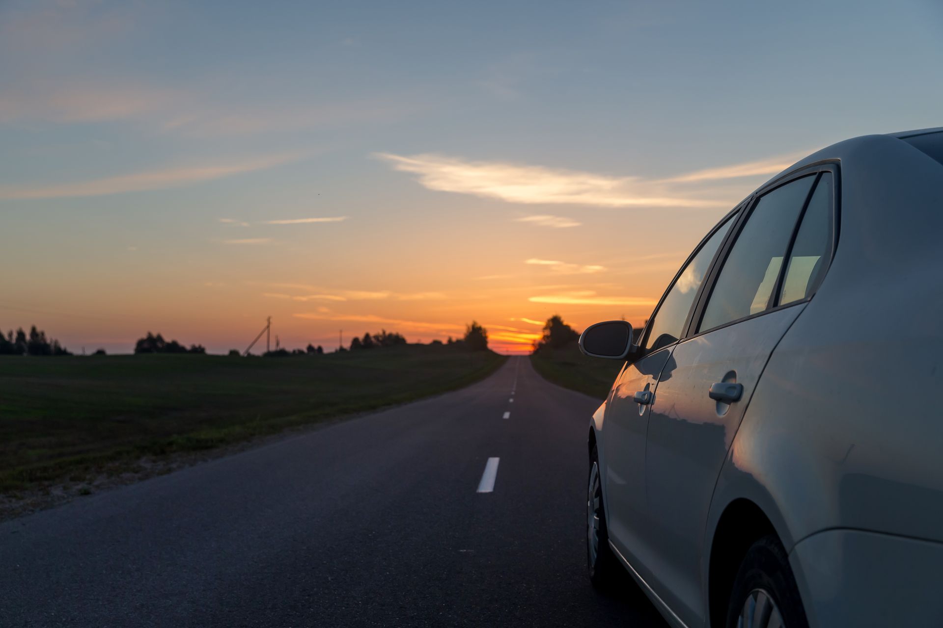 A car is parked on the side of the road at sunset. 