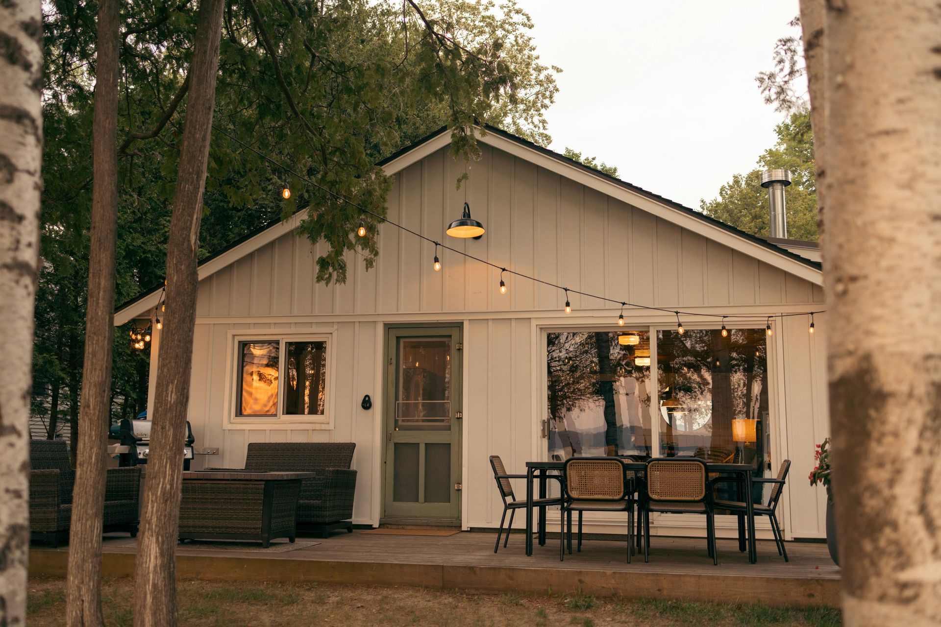A white house with a patio and a string of lights hanging from the roof. 