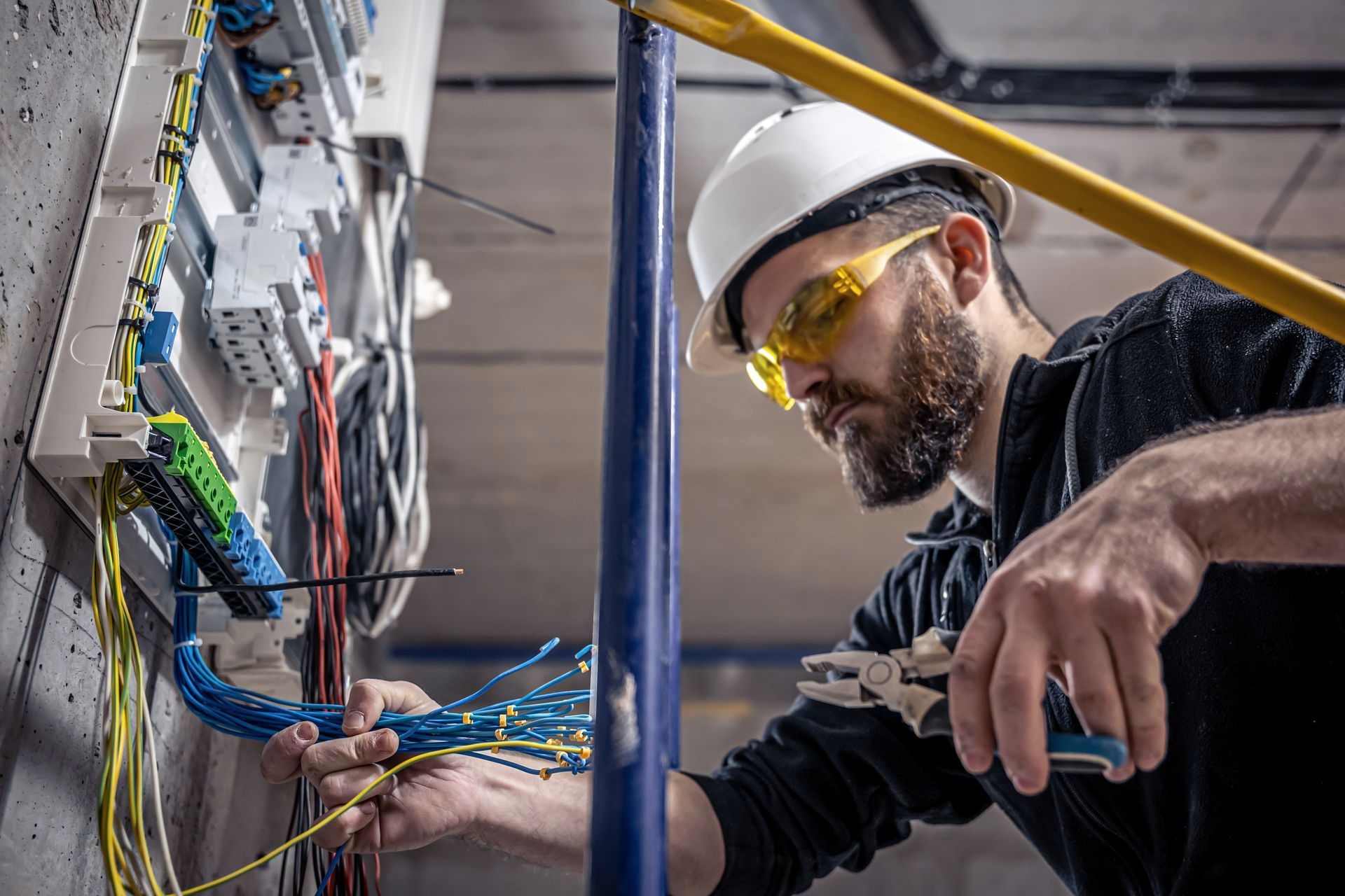 A man wearing a hard hat and safety glasses is working on an electrical panel. 