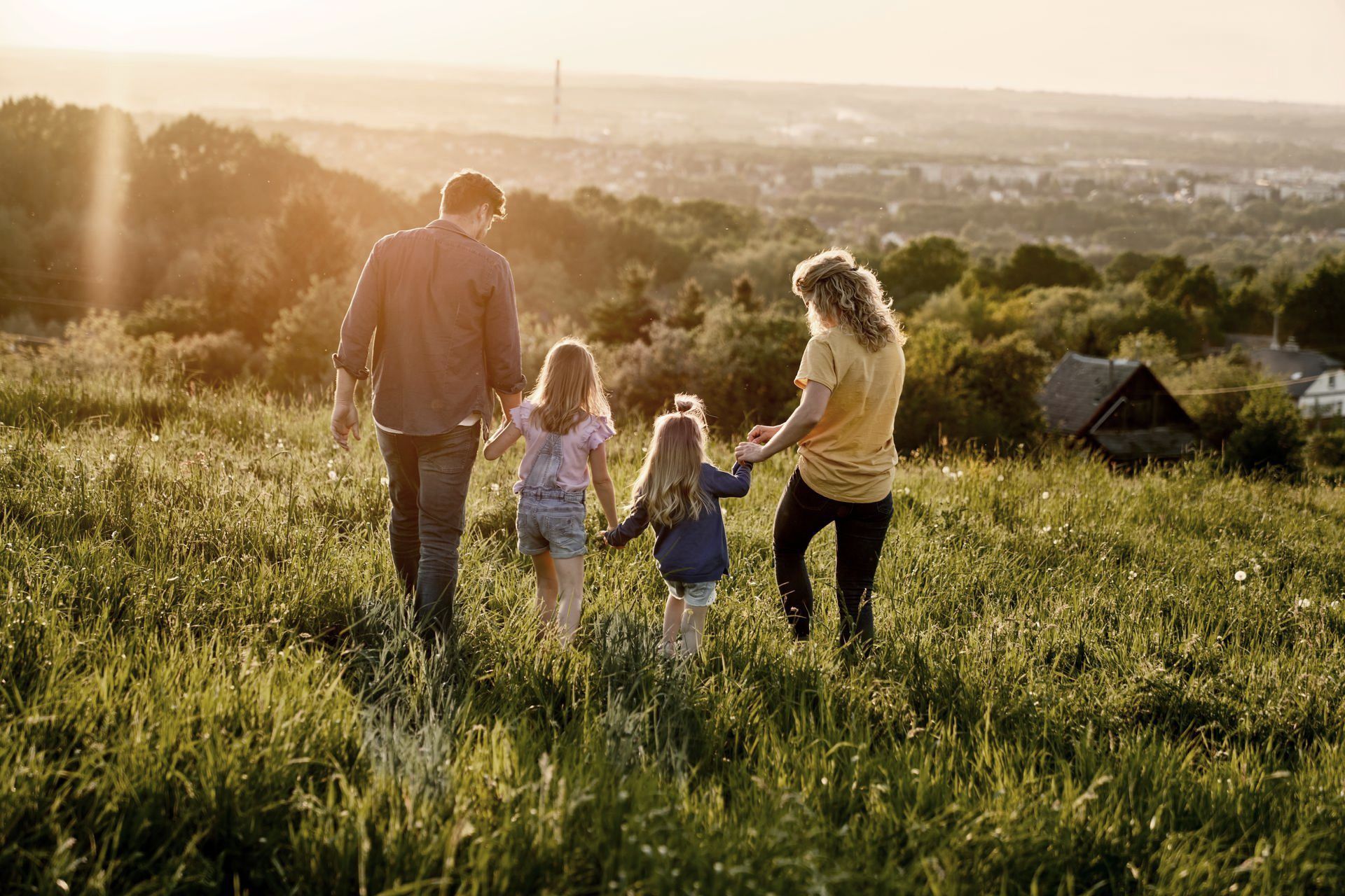 A family is walking through a grassy field holding hands.