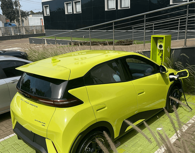 Um carro elétrico hatchback amarelo brilhante estacionado e conectado a uma estação de carregamento verde-limão.