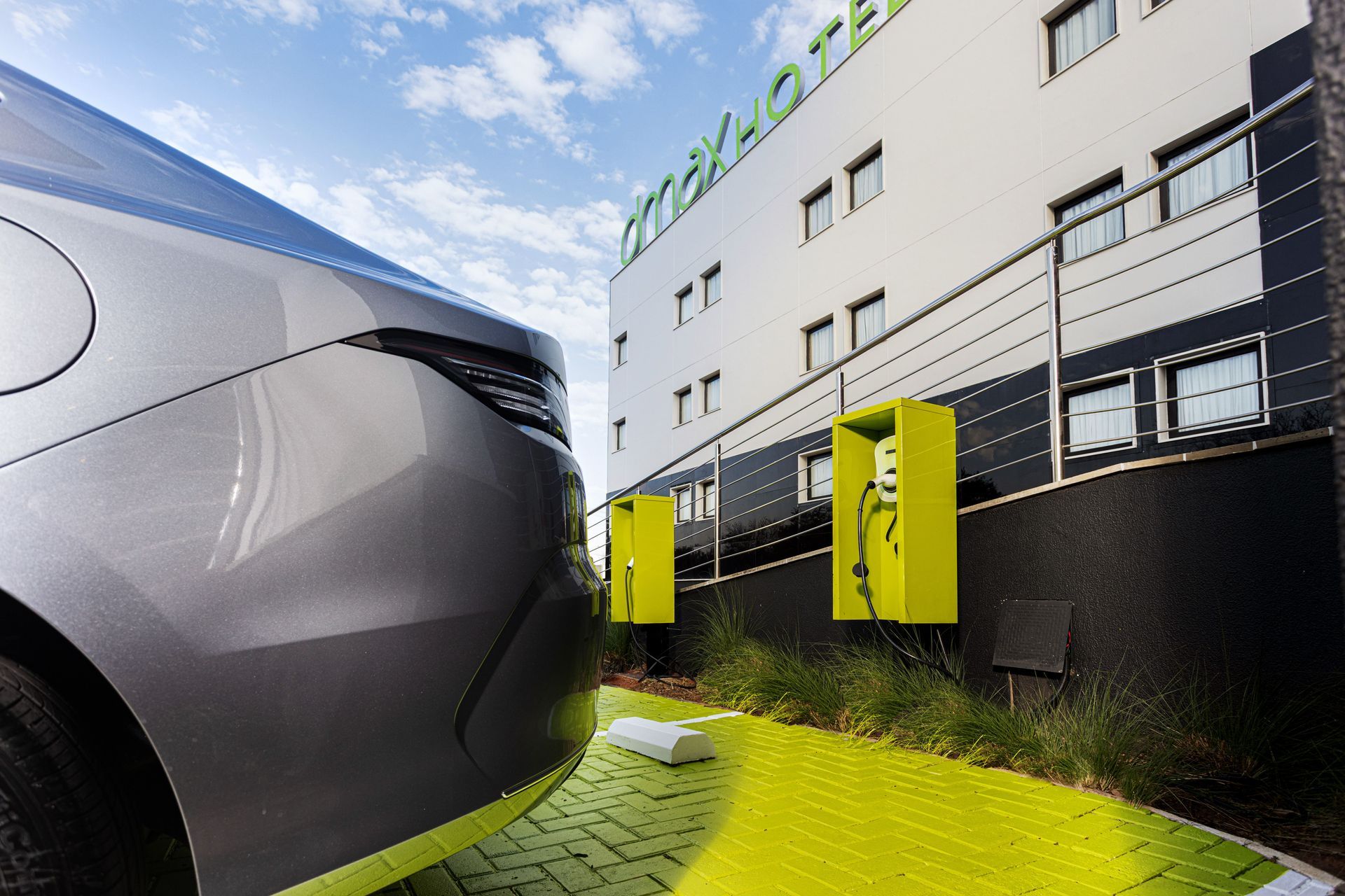 Um carro elétrico prateado estacionado em um hotel d'max ao lado de estações de carregamento verde-limão brilhantes em um estacionamento pavimentado e pintado.