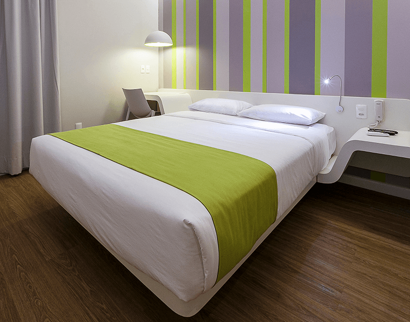 Um quarto com uma cama de casal queen-size, lençóis brancos, um tapete verde-limão, papel de parede listrado e uma escrivaninha moderna.