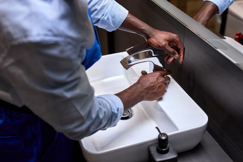 Person using a wrench to install a kitchen faucet over a stainless steel sink