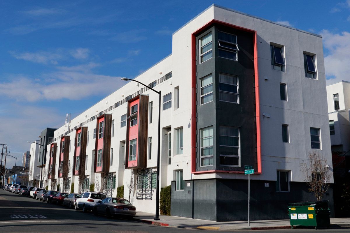 A large apartment building with cars parked in front of it on a sunny day.