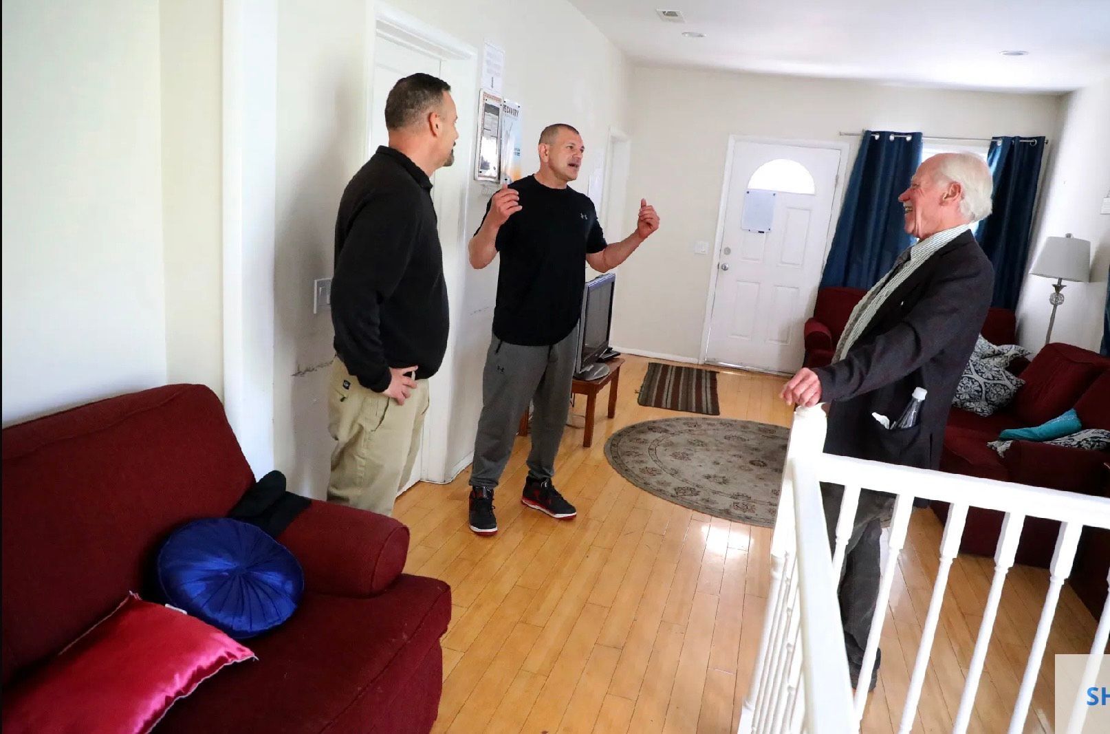 Three men are standing in a living room talking to each other