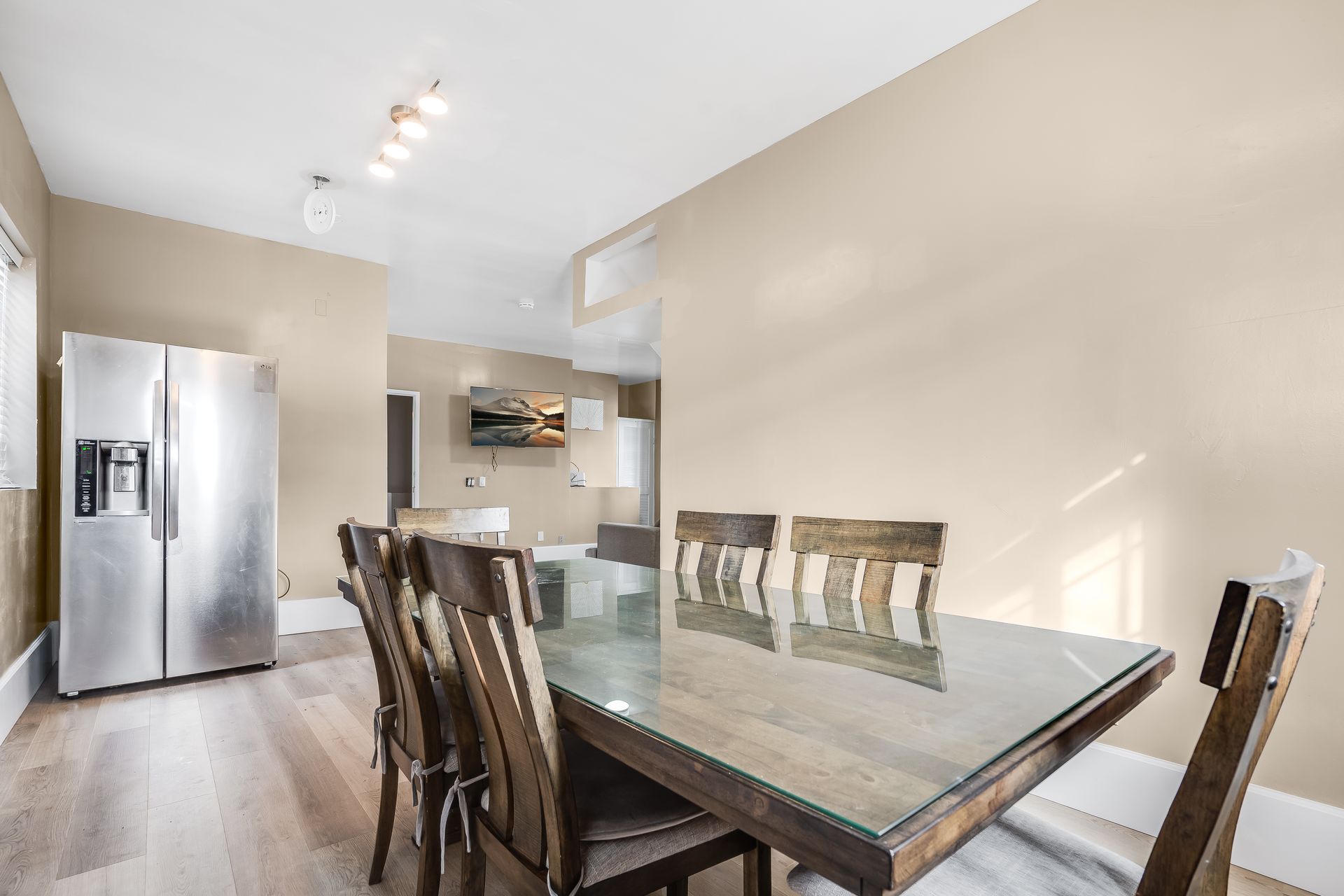 A dining room with a glass table and chairs and a refrigerator.