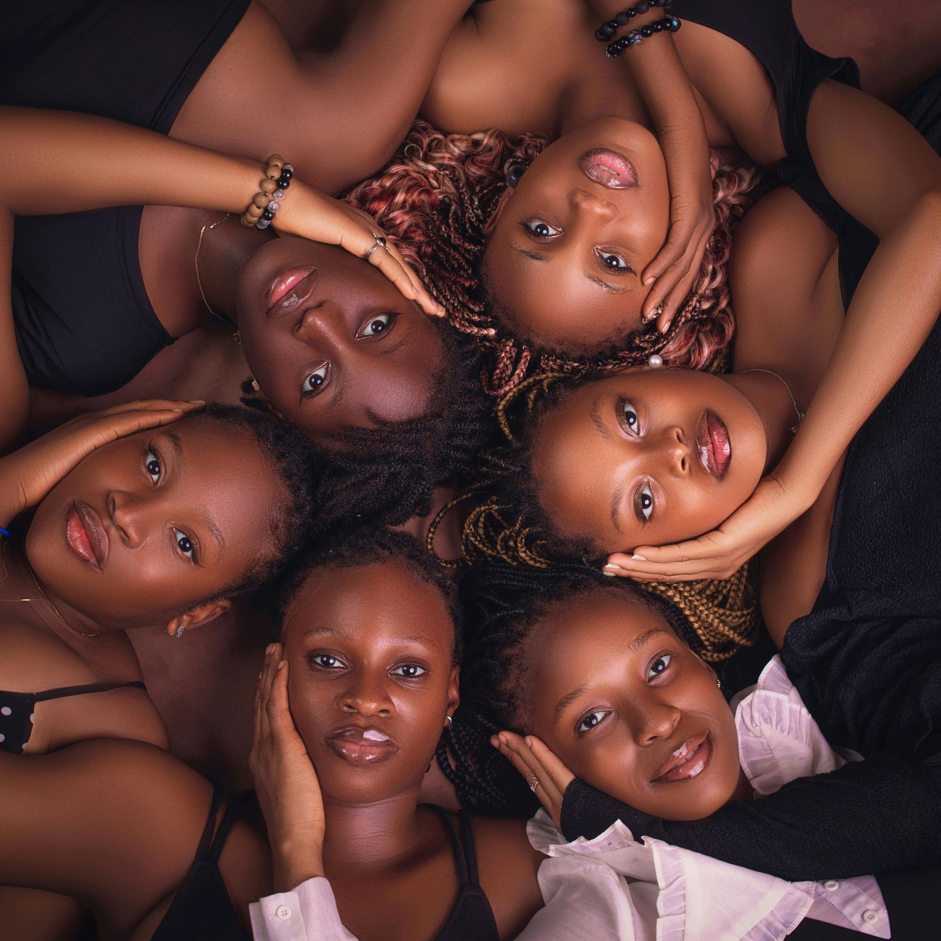 A group of women are laying in a circle with their hands on their faces