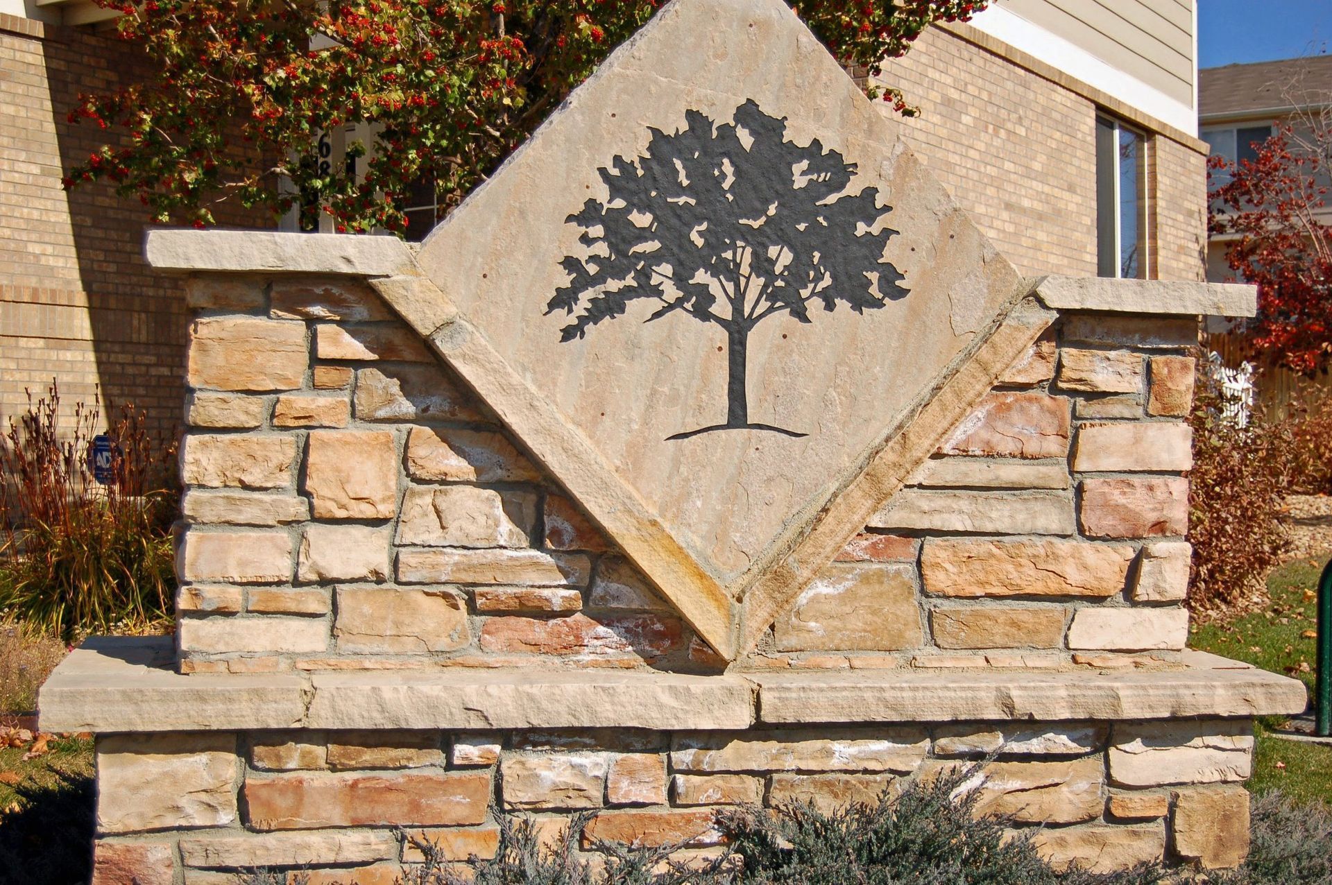 Stone monument sign with a black tree logo on a tan diamond panel, set in a landscaped outdoor entrance
