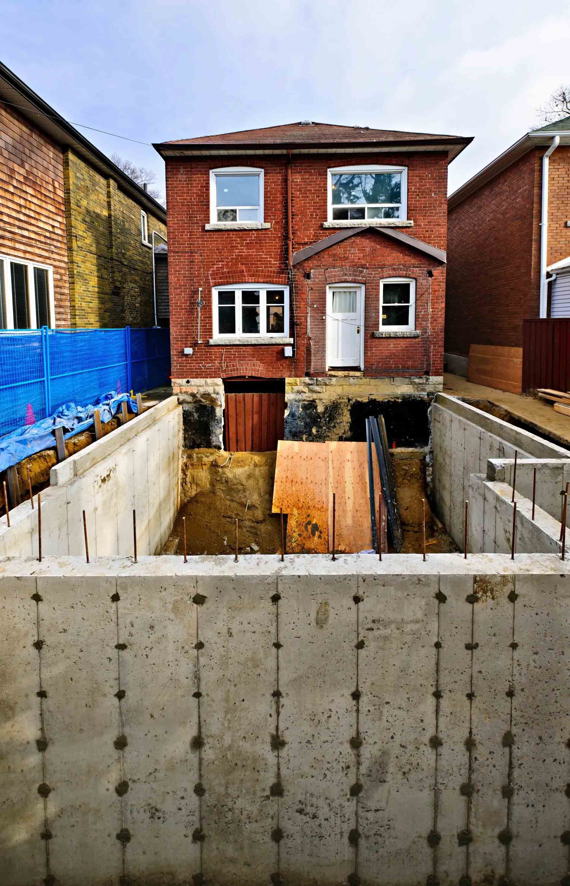Fondations de maison partiellement construites à côté d'une maison en briques rouges avec excavation et murs en béton