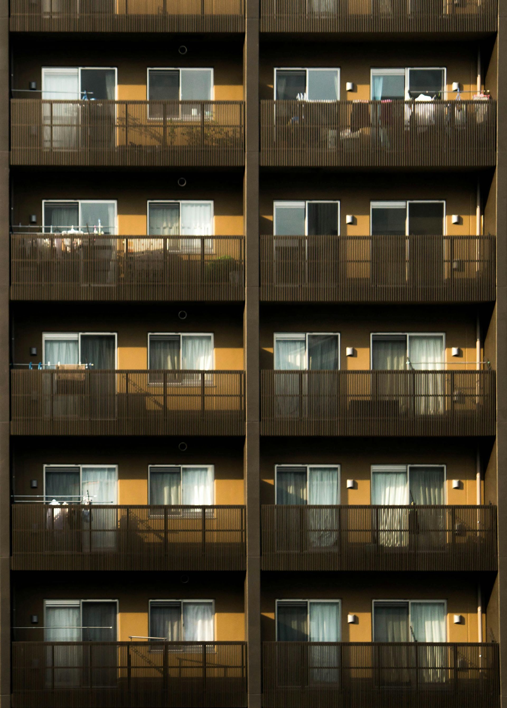 A multistory apartment building facade featuring identical balconies and sliding glass doors, arranged in a grid pattern.