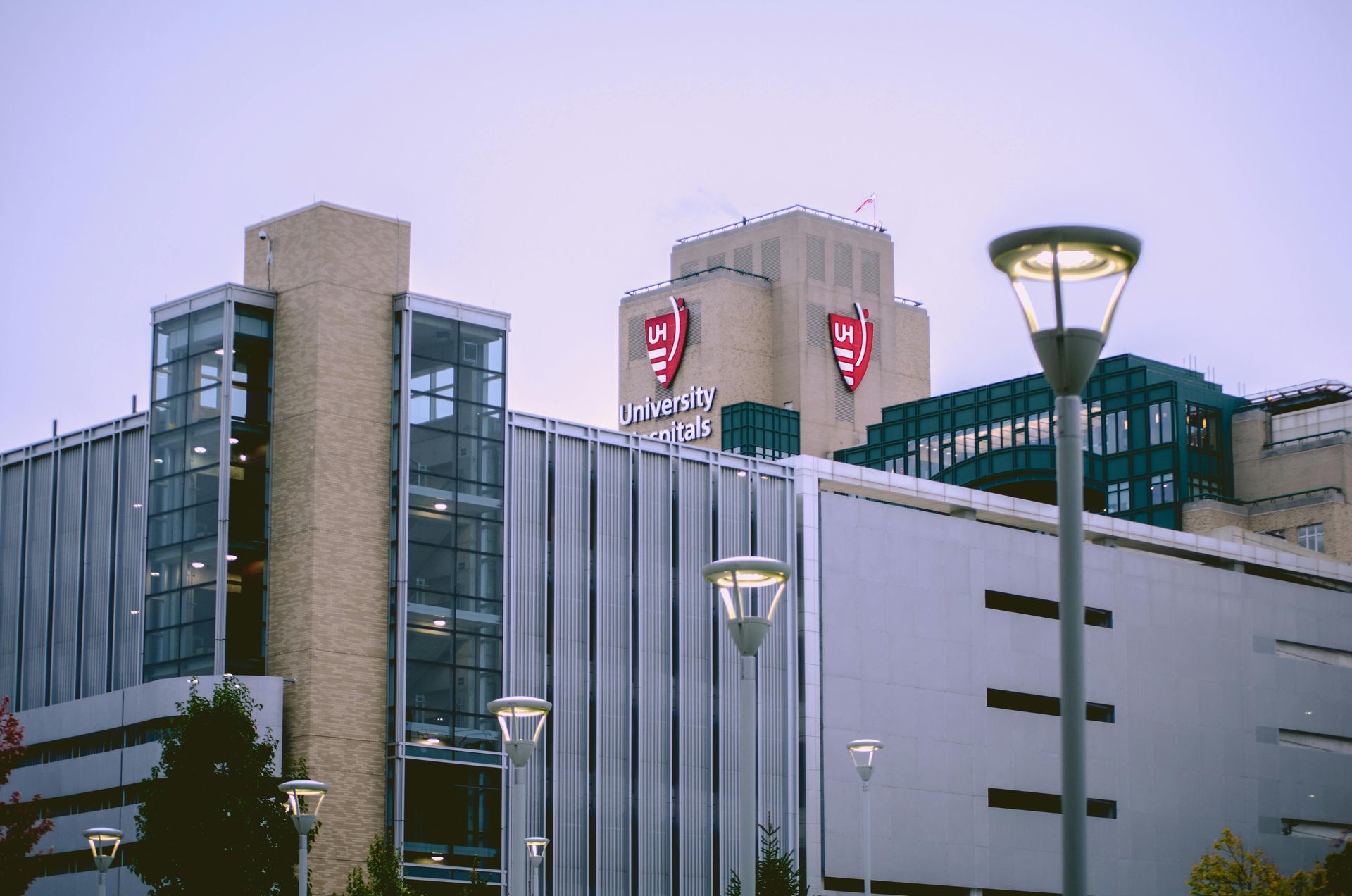 A modern parking garage with a tan stone tower and two red shields featuring white letters under a pale sky.