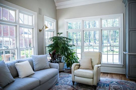 Sunroom with light gray sofa, cream recliner, large windows, and leafy plant.