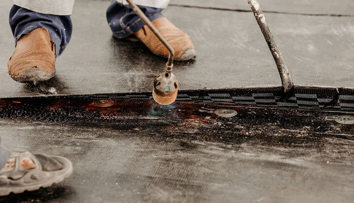 Person using a torch to seal seams on a black roofing surface.