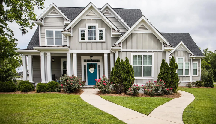 Gray house with white trim, teal door, and a walkway through a green lawn.