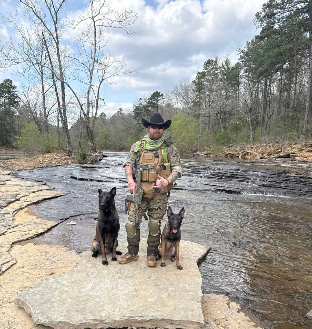 Soldier in camouflage with a black military dog in a leaf-covered forest