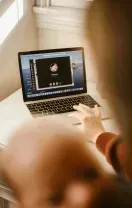 A person’s hand rests on a laptop keyboard while participating in a video call on a desk near a window.