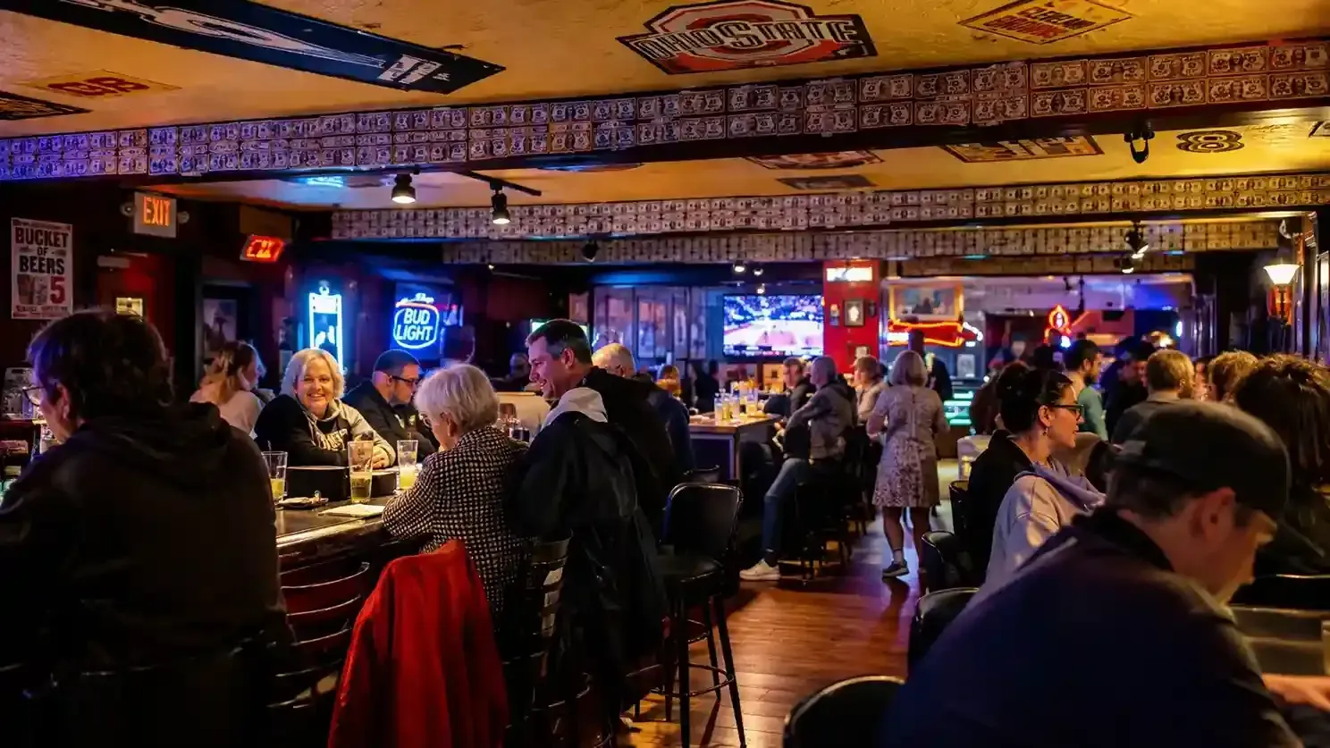Crowded bar with patrons seated at tables under warm neon lights and TVs, lively nighttime atmosphere
