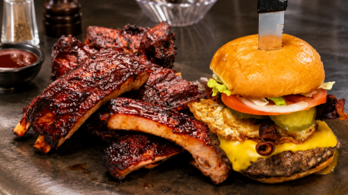 BBQ bacon cheeseburger with onion rings and glazed ribs on a dark plate