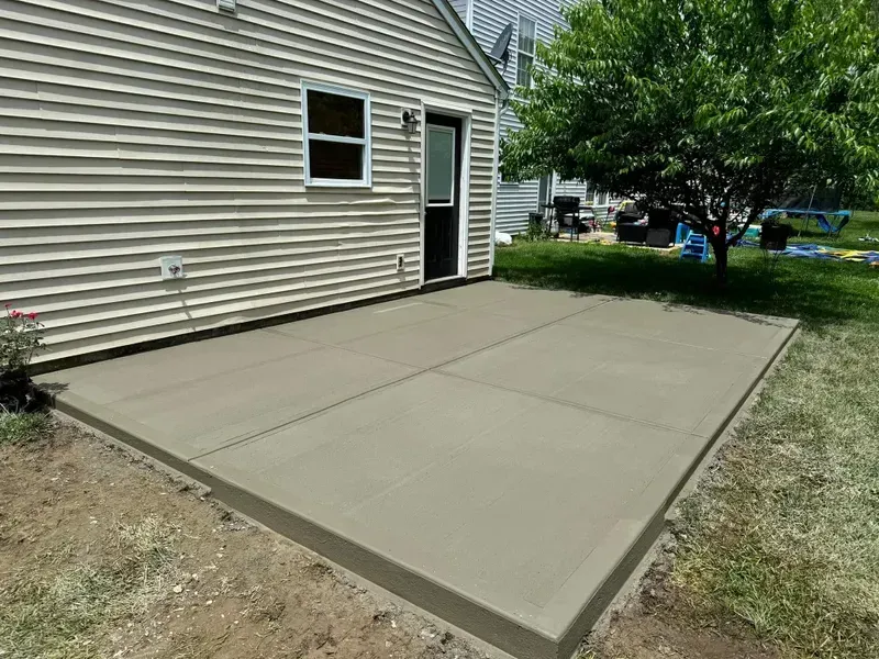 Concrete patio beside a beige house, with a door and window opening onto a backyard.