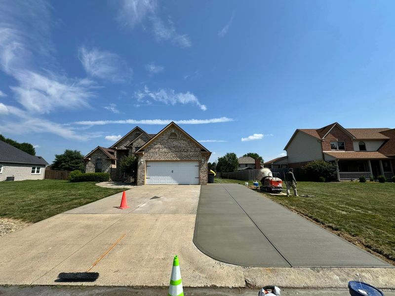 Suburban house with a driveway under construction, orange and green cones, and parked car on the right