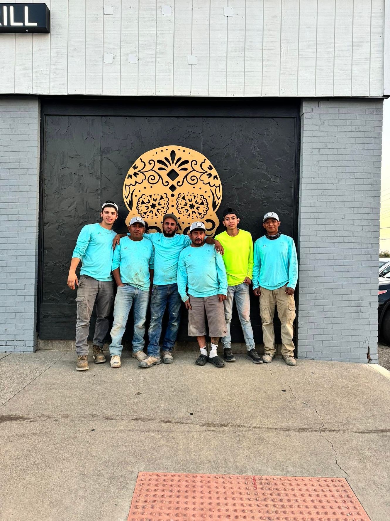 Six people in matching blue shirts stand in front of a gray building with a circular wall mural.