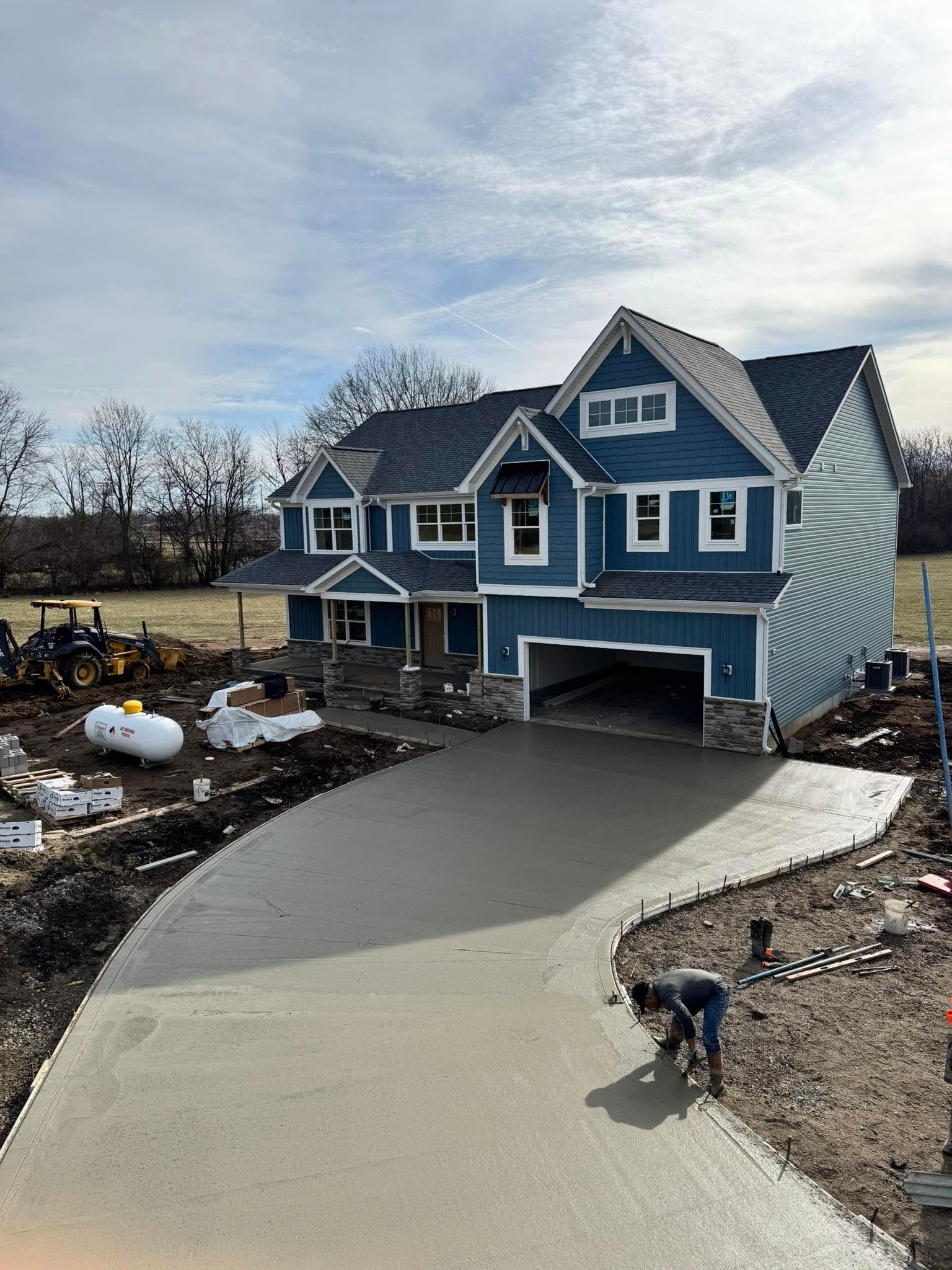 Blue house with a new concrete driveway under construction; a worker stands on the driveway in front.
