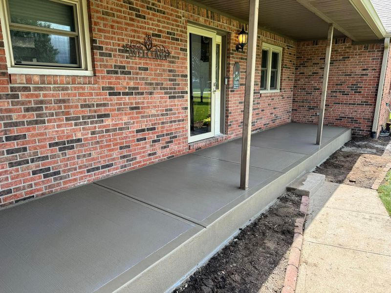 Concrete accessible walkway along brick house porch with a central support post and door.