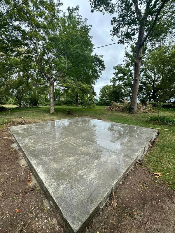 Concrete slab in a grassy park, surrounded by trees and wet with puddled rainwater.