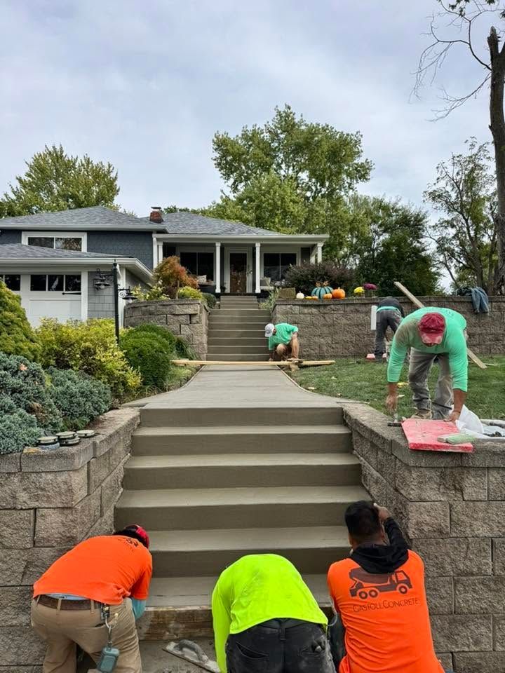 Workers painting outdoor steps and retaining walls in a landscaped front yard.