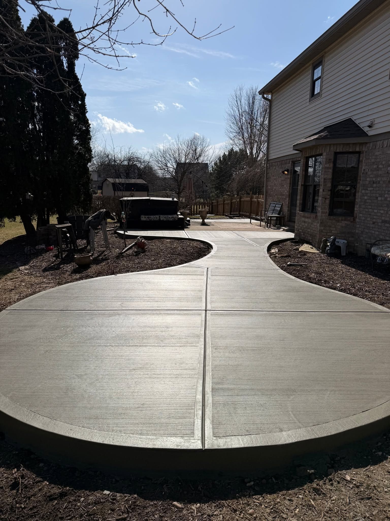 Concrete curved walkway beside a house and landscaped garden under a sunny sky