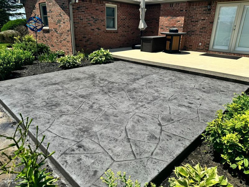 Stamped concrete patio beside a brick house with a raised wooden deck and garden beds.