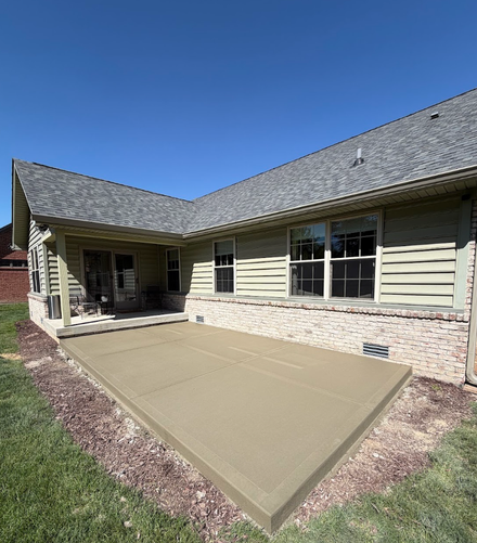 Fresh concrete patio beside a beige house, with a door and windows overlooking a backyard.