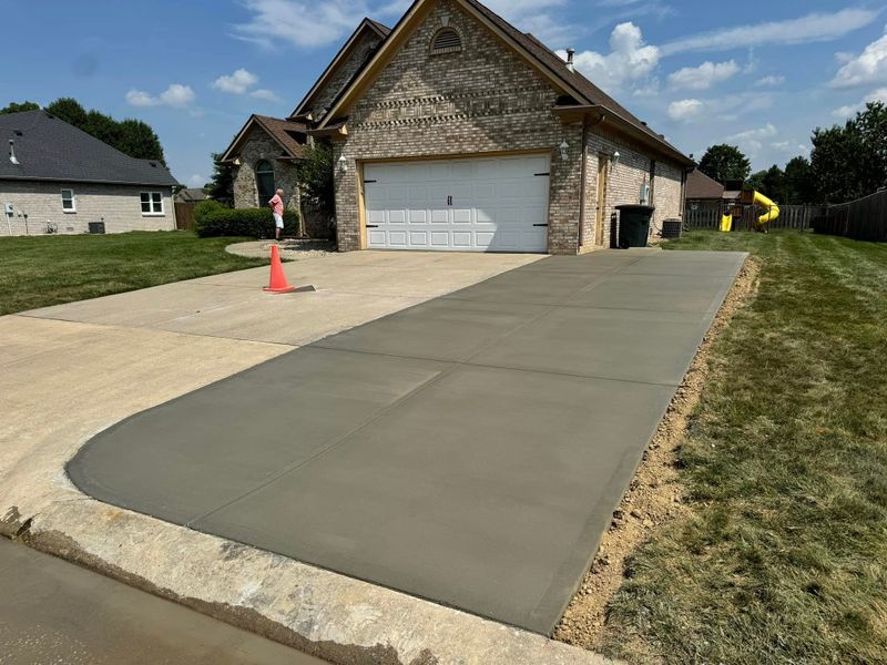 New concrete driveway beside a garage with an orange cone and curb edges under construction