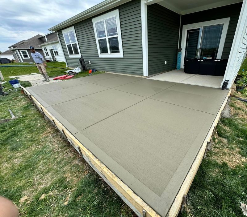 Freshly poured concrete patio beside a house, with a worker in the background