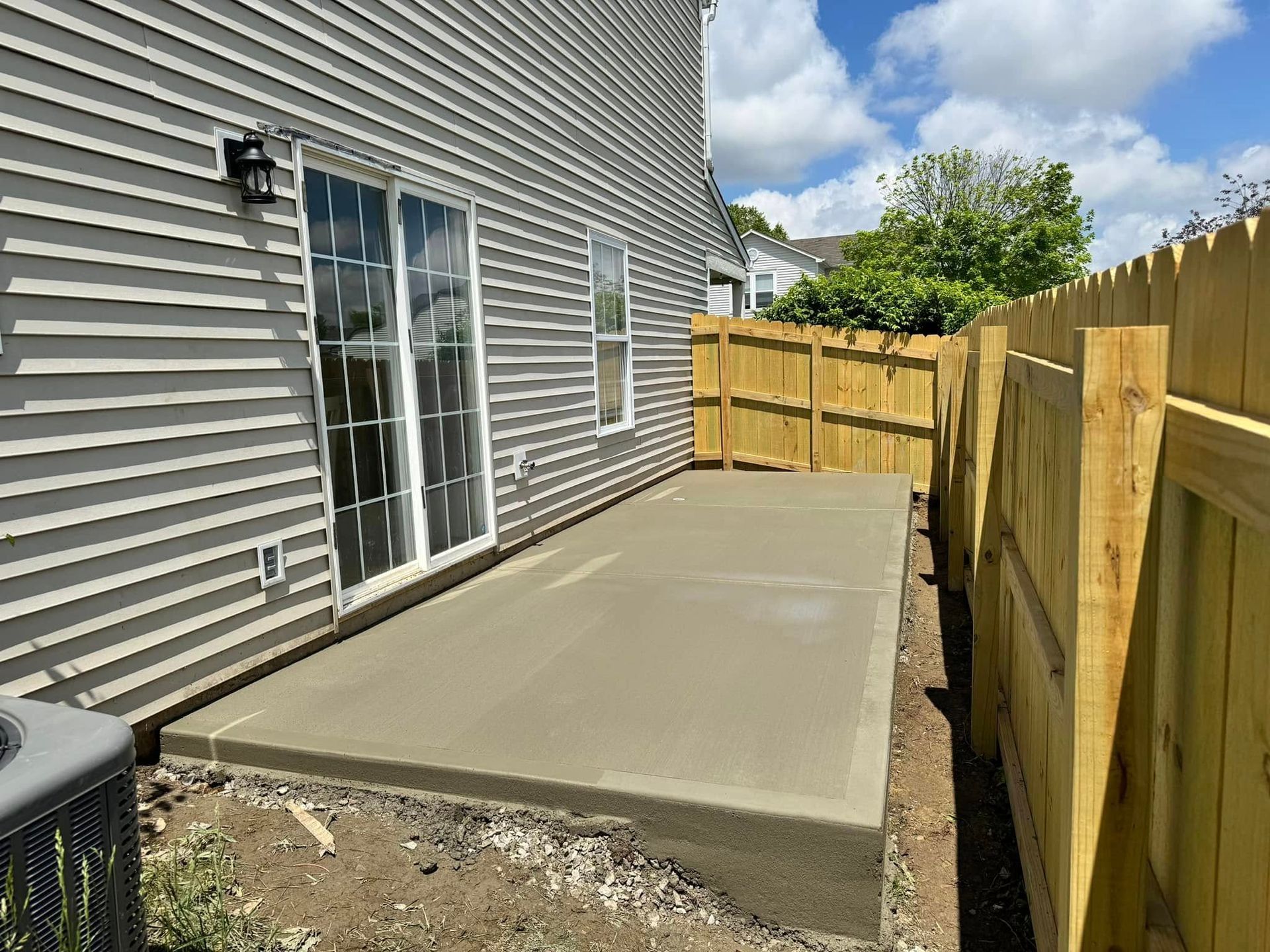 Concrete patio beside house with sliding glass door and wooden privacy fence.