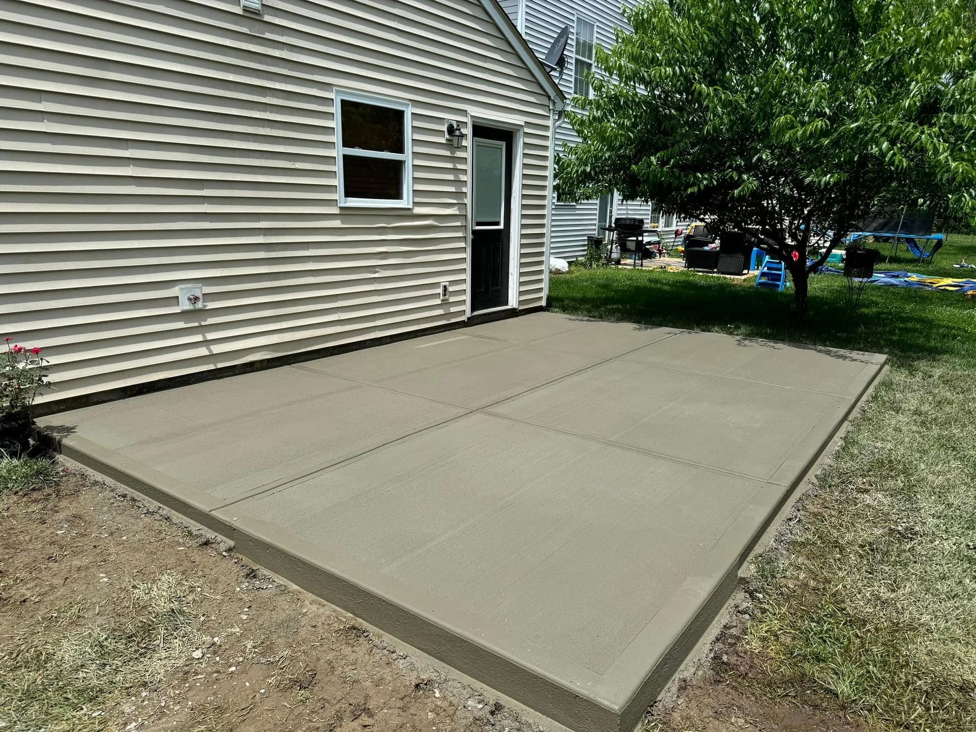 Concrete patio beside beige house with open side door and grassy yard.